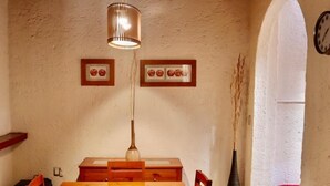 A dining area with a wooden table and chairs, a hanging light fixture, framed pictures on the wall, and a clock.