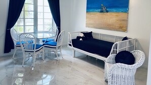 A room with a dining table and chairs, a white wicker sofa, a ceiling fan, and a beach painting on the wall.