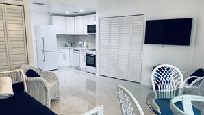 A modern kitchen with white cabinets, a built-in oven, and a microwave. There is a dining area with a glass table and white chairs.