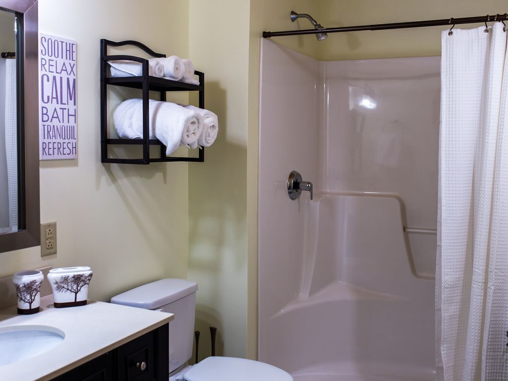 Un baño con ducha, inodoro y lavabo. Hay un perchero con toallas y un cartel que dice 