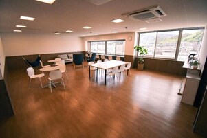 Un salón de conferencias con una gran mesa y sillas, un sofá y vistas a un paisaje urbano a través de amplios ventanales.