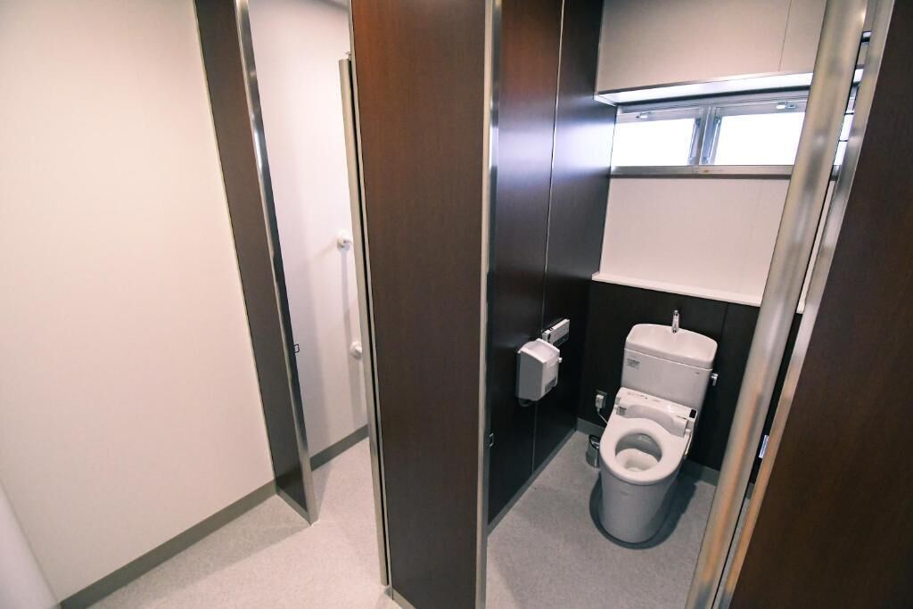 A compact, modern bathroom with a toilet, a hand dryer, and a paper towel dispenser.