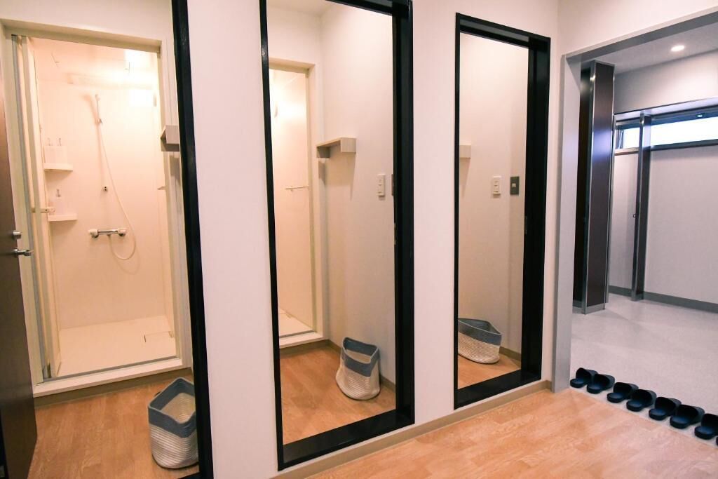Un pasillo con pared espejada, zona de ducha y zapatero con varios pares de zapatos.