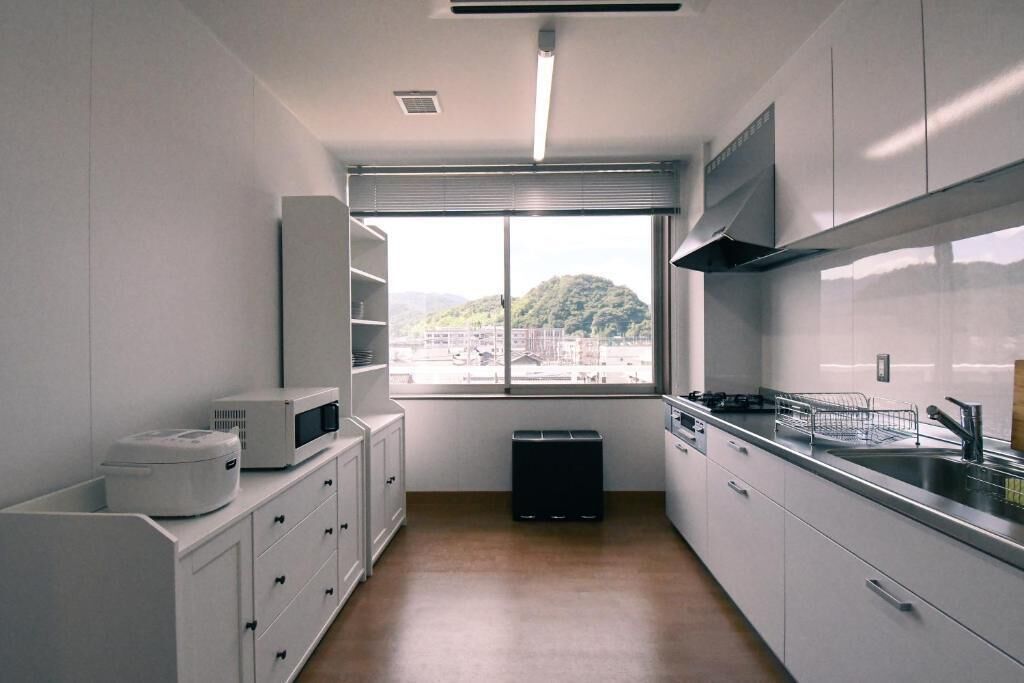 Cocina compacta con armarios blancos, microondas, fregadero y ventana con vistas a la montaña.