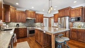 Una cocina con armarios de madera, refrigerador de acero inoxidable, microondas y encimera de granito.