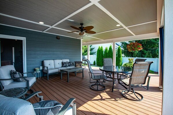 An outdoor patio with a ceiling fan, a dining table with chairs, and a sofa set.