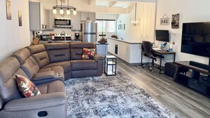A modern living room with a sectional sofa, a flat-screen TV, and a small kitchen area in the background. - Renovated & spacious 2 bed/2 bath Condo with Mountain Views - near Eagle Lodge  (Mammoth Lakes)