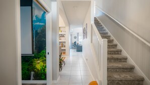 A modern interior with a staircase, a hallway leading to a living area, and a view of greenery through a glass door.
