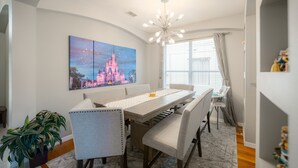 A dining area with a long table, chairs, and a chandelier.