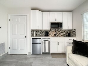 A compact kitchen with white cabinets, a microwave, a refrigerator, and a dishwasher.