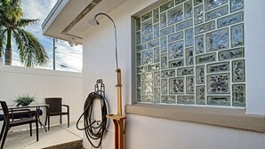 Un patio con una mesa y sillas de madera, una planta en maceta, una manguera y un cabezal de ducha montado en la pared.