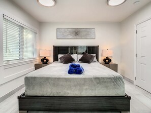 A modern bedroom with a large bed, two bedside tables, a ceiling light, and a window with blinds.