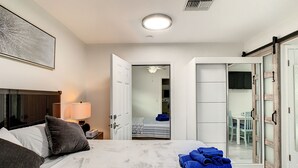 Habitación de hotel con cama, mesita de noche, lámpara, ventilador de techo y vista a otra habitación.