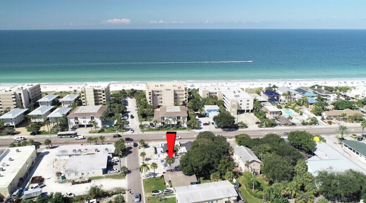 A coastal hotel area with multiple buildings, a beach, and a road.