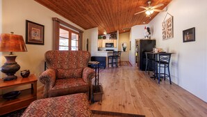 Un salon chaleureux avec un fauteuil à motifs, un plafond en bois et un coin repas comprenant des chaises et une table.