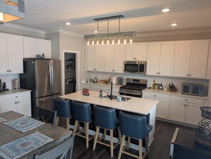 A modern kitchen with white cabinets, stainless steel appliances, a central island with bar stools, and a pendant light fixture.
