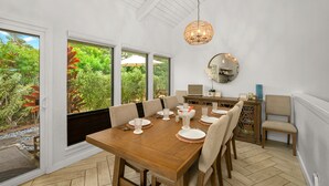 Un coin repas avec une table en bois dressée pour six personnes, de grandes fenêtres et un luminaire suspendu.