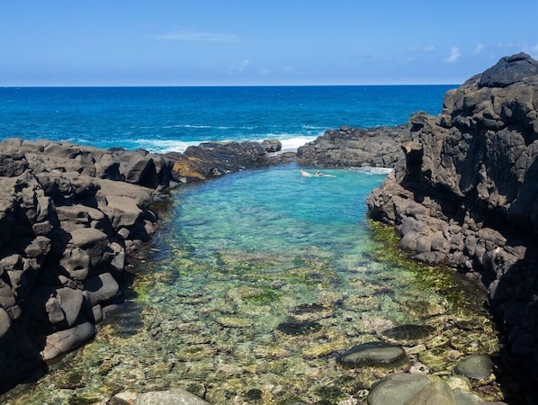 A rocky coastal area with clear water, a view of the ocean, and a person swimming. - Hawaiian Bungalow ~A/C~ BBQ~ Near Beaches & Shops (Princeville)