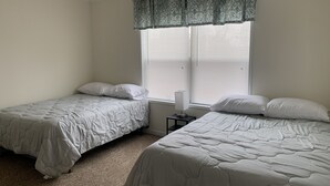 Une chambre avec deux lits, une table de chevet et une fenêtre avec des stores.