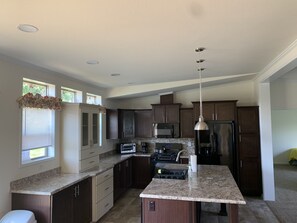 A modern kitchen with dark wood cabinets, granite countertops, a stainless steel refrigerator, and a built-in oven. - Buck House By The Bay- 4 Season Rural Cozy Cabin (Sturgeon Bay)