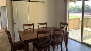 Un coin repas avec une table et des chaises en bois, et une porte-fenêtre coulissante donnant sur une terrasse extérieure.