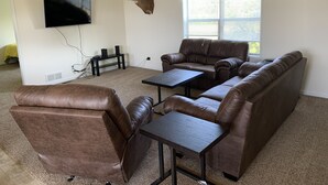 Un salon avec un canapé en cuir marron, une table basse, un téléviseur à écran plat fixé au mur et un ventilateur de plafond.