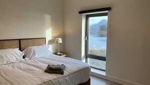Una camera da letto con un letto, un comodino, una lampada e vista su un lago attraverso una porta scorrevole.