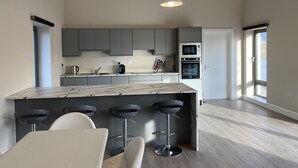 Una cucina moderna con mobili grigi, un'isola in marmo con sgabelli da bar ed elettrodomestici integrati.