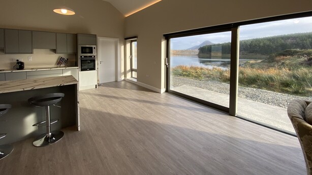 Una cucina moderna con una grande isola, elettrodomestici integrati e vista su un lago e una foresta.