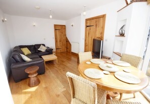 A modern living room with a sofa, coffee table, dining table with placemats, and a TV.