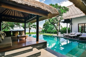 A poolside area with a thatched roof structure, outdoor seating, and a view of the ocean.