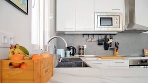 A modern kitchen with white cabinets, a stainless steel microwave, and a sink with a faucet. There is a wooden crate with fruits and a kettle on the counter. - Stunning renovated 2-Bed Apartment in Valencia (València)
