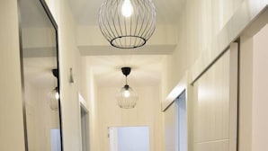 A hallway with a mirrored wall, a ceiling light fixture, and a chair in the distance. - Stunning renovated 2-Bed Apartment in Valencia (València)