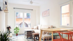 A bright living room with a sofa, a wooden table, and chairs. There is a window with a view of buildings outside. - Stunning renovated 2-Bed Apartment in Valencia (València)