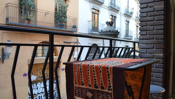 A balcony with a patterned tablecloth, a metal railing, and a view of adjacent buildings with balconies and potted plants. - Stunning renovated 2-Bed Apartment in Valencia (València)