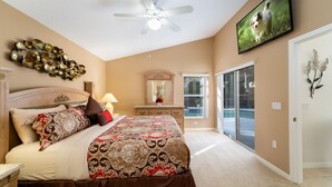 A bedroom with a bed, a ceiling fan, a TV, a dresser, and a large window. - Pool Home In Gated Community Close to Disney (Davenport)
