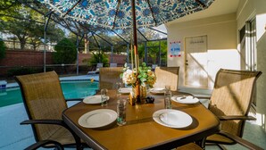An outdoor dining area with a table set for four, surrounded by wicker chairs, under a patterned umbrella. - Pool Home In Gated Community Close to Disney (Davenport)