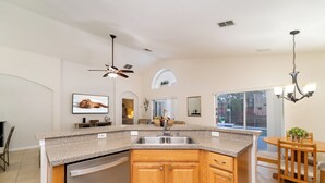 A kitchen with a granite countertop, wooden cabinets, a dishwasher, a ceiling fan, and a dining area with a table and chairs. - Pool Home In Gated Community Close to Disney (Davenport)