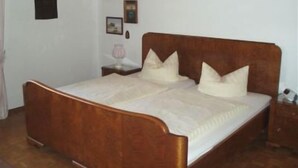 A wooden bed with a headboard, a bedside table, and a nightstand with a lamp. - Vacation apartment for up to 4 people, 90 sqm, 2 large bedrooms, balcony (Piding)
