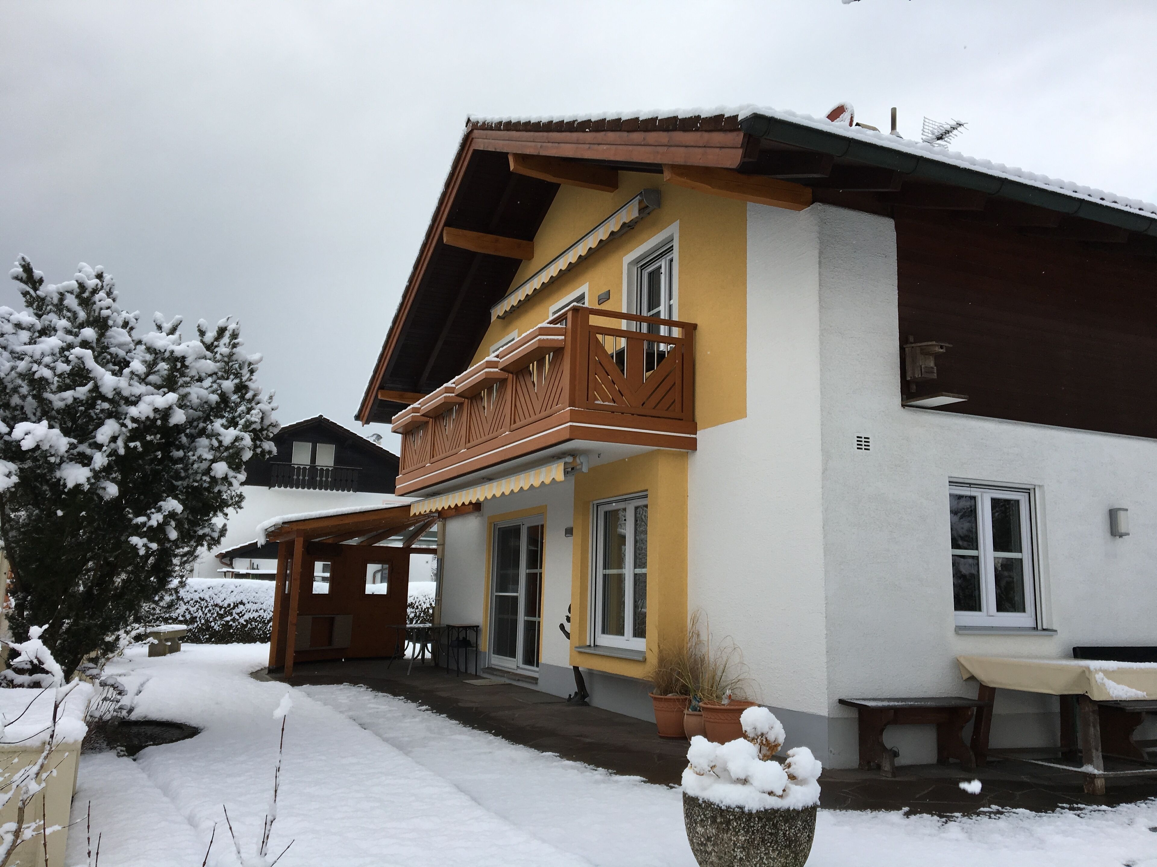 A two-story building with a balcony, a covered porch, and a snow-covered garden.