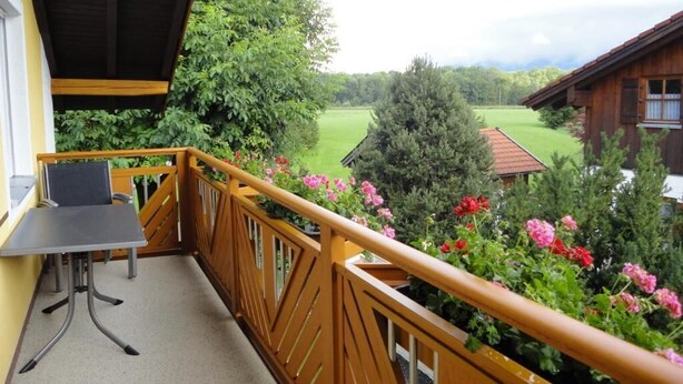 A balcony with a table and chairs, overlooking a green landscape with trees and a building. - Vacation apartment for up to 4 people, 90 sqm, 2 large bedrooms, balcony (Piding)