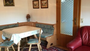 A dining area with a table and benches, a red chair, and a door with a textured glass panel. - Vacation apartment for up to 4 people, 90 sqm, 2 large bedrooms, balcony (Piding)