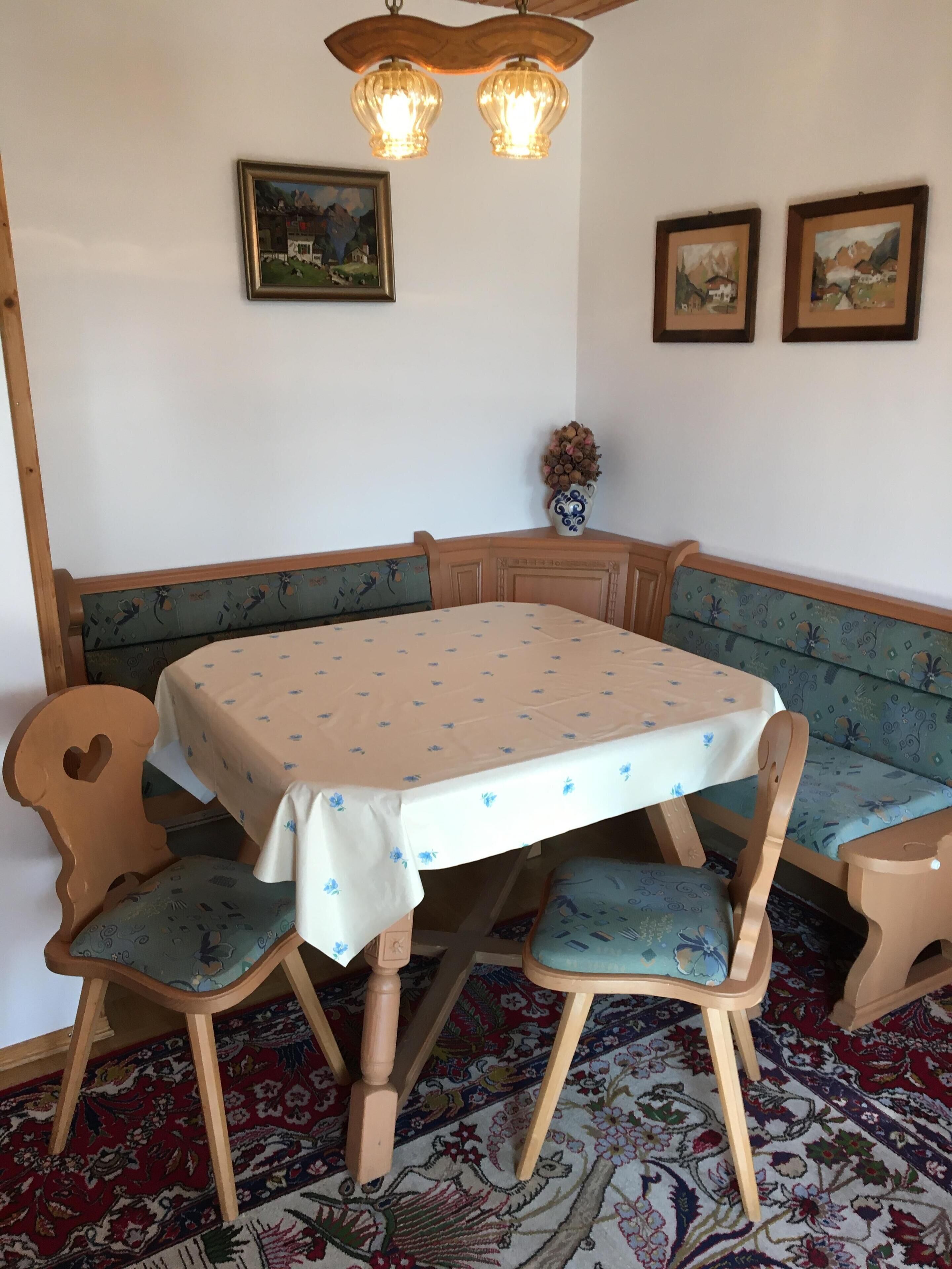 Un coin repas avec une table ronde recouverte d’une nappe à motifs floraux, entourée de chaises en bois avec des coussins à motifs.