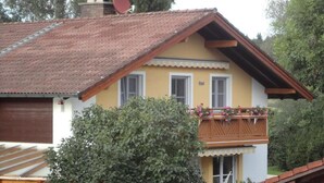 A two-story house with a balcony, surrounded by greenery. - Vacation apartment for up to 4 people, 90 sqm, 2 large bedrooms, balcony (Piding)