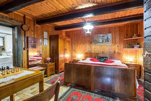 Ein Zimmer mit Holzboden, einem Bett, einem Schreibtisch mit Schachfiguren und einem Gemälde an der Wand.