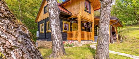A wooden cabin with a porch, surrounded by trees.