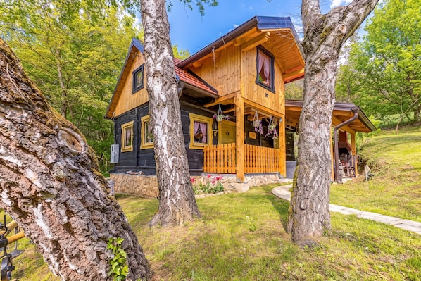 A wooden cabin with a porch, surrounded by trees.
