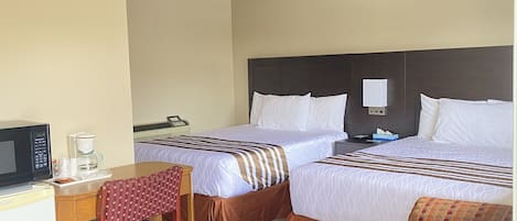 A hotel room with two beds, a desk with a microwave, a chair, and a small table with a coffee maker.