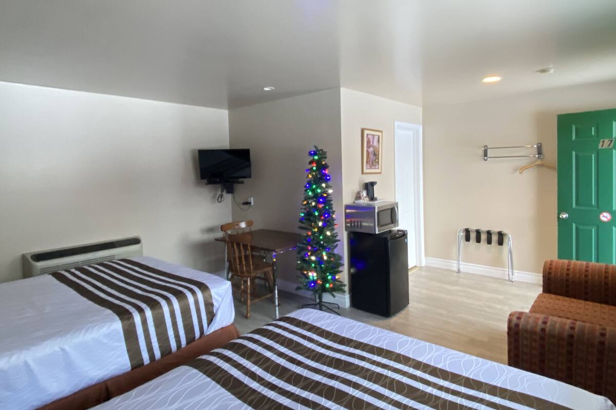 A hotel room with two beds, a TV, a Christmas tree, a dining table, and a microwave.