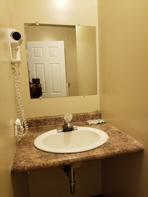 Un baño con un lavabo blanco, un espejo y un secador de pelo montado en la pared.